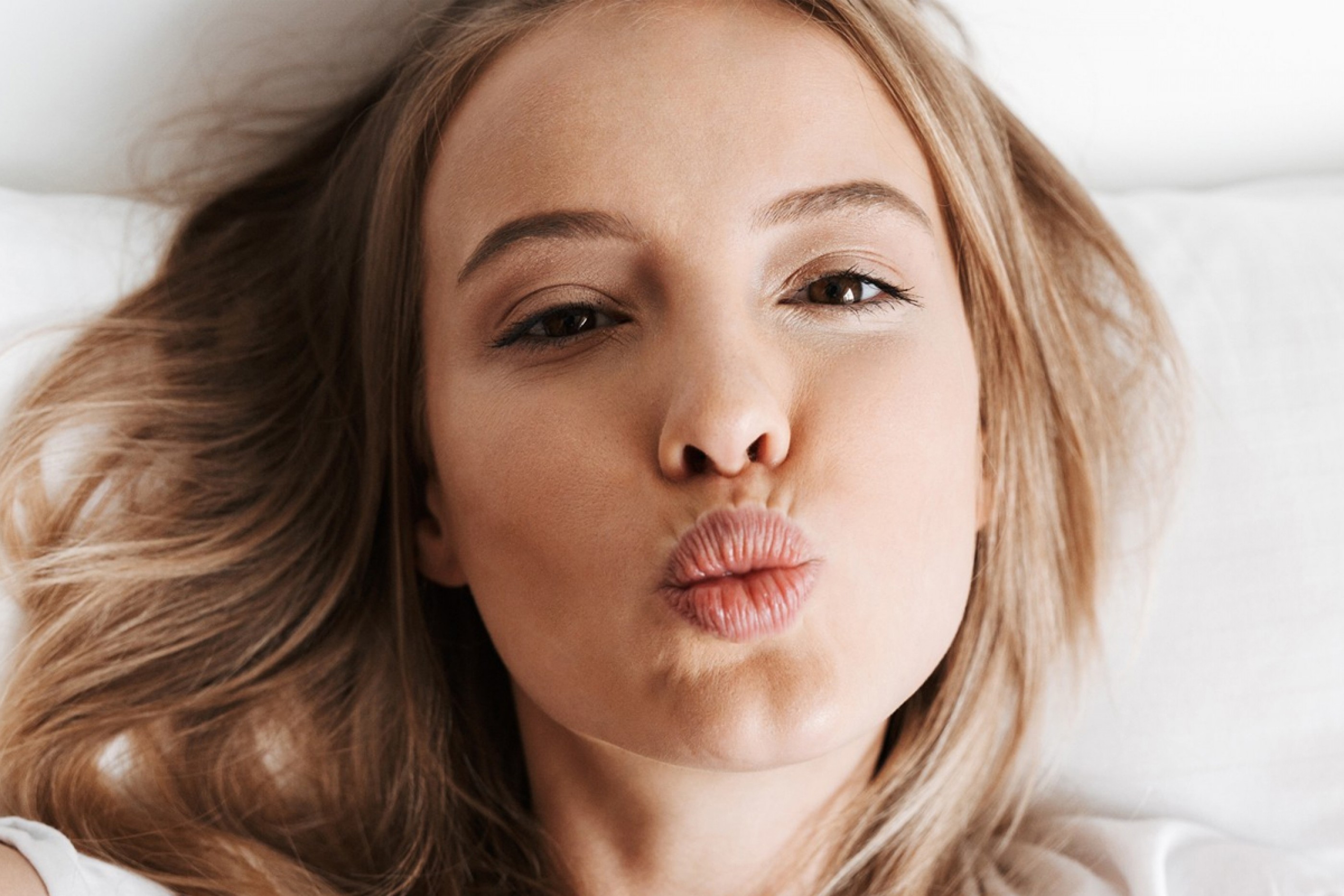 Young woman puckering lips after dermal filler treatment for lip and cheeks enhancement.
